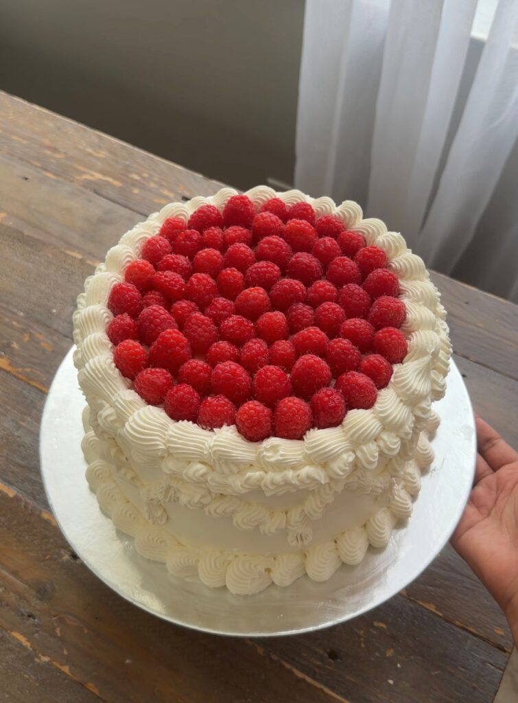 Vintage-style white frosted cake topped with bright red cherries and detailed buttercream swirls on a cake stand.