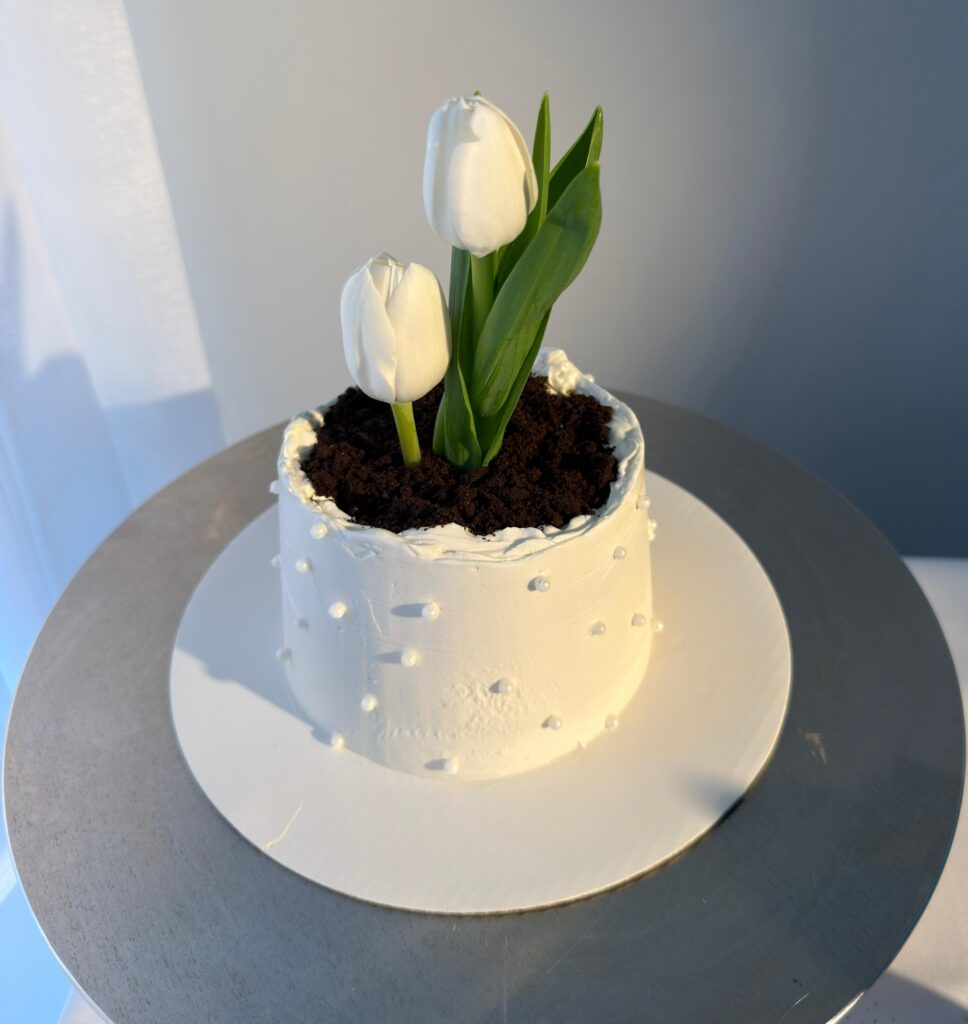 Artistic buttercream cake decorated with fresh tulips, chamomile flowers, and lemon slices in soft natural lighting.