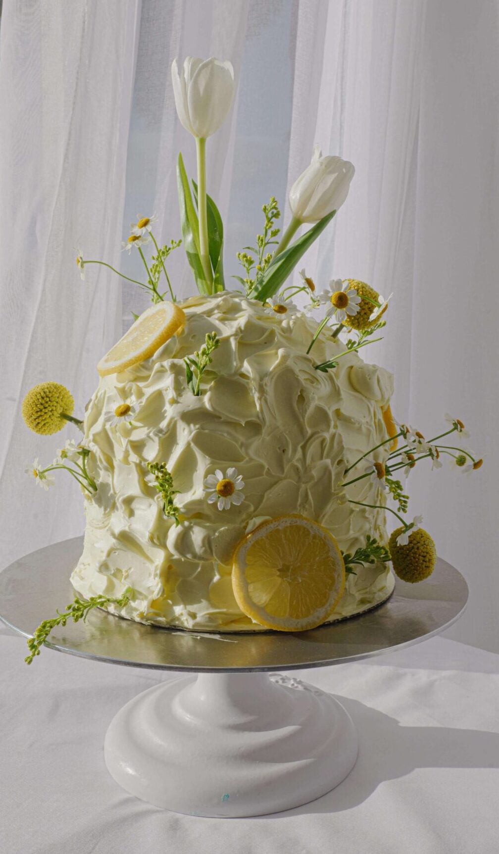 Minimalist white mini cake topped with fresh white tulips and chocolate crumble for a modern floral cake design.
