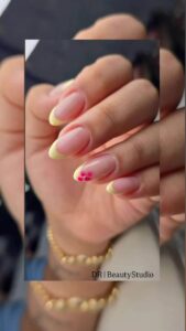 Natural almond-shaped manicure with soft yellow French tips and delicate floral nail art by DR Beauty Studio.