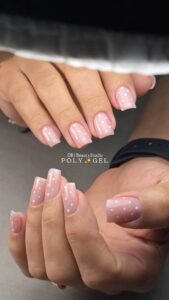 Natural-looking French manicure with glossy pink almond-shaped nails and curved white tips by DR Beauty Studio.