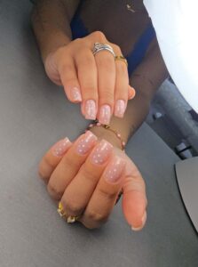 Glossy soft pink manicure with white polka dot nail art and clean square-shaped nails by DR Beauty Studio.