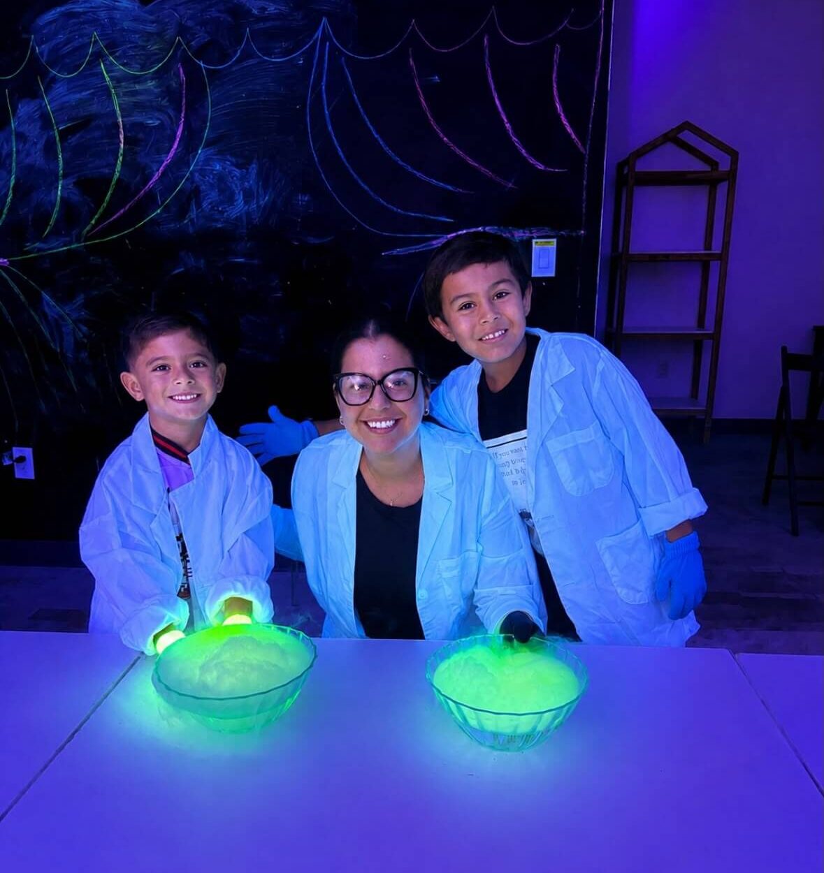 Children participating in an immersive Bilingual STEAM science activity under colorful UV lighting, experimenting with glowing materials and hands-on sensory elements
