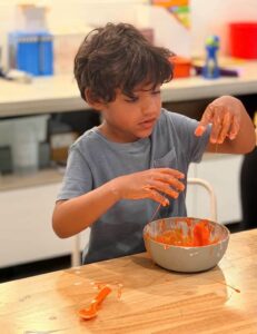 Student exploring a colorful hands-on science experiment during a bilingual English-Spanish Future Minds Little Scientist STEAM class.